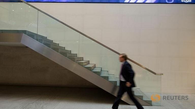 A man walks under an electronic information board at the London Stock Exchange in the City