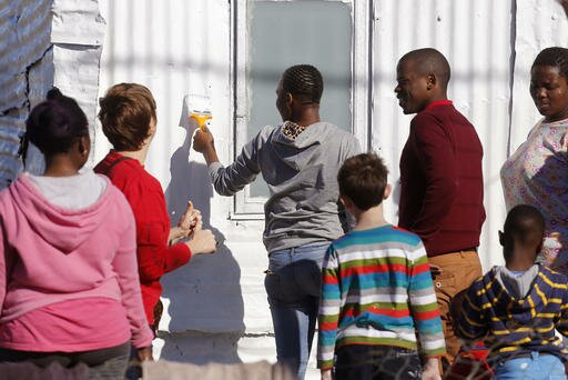 A woman center paints a shack with white fire retardant paint as part of their contribution to International Nelson Mandela Day in the township of Nomzamo South Africa