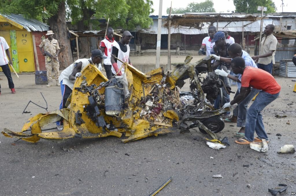 People inspect a damaged tricycle at the site of a bomb explosion caused by a female suicide bomber in a market in Maiduguri Nigeria